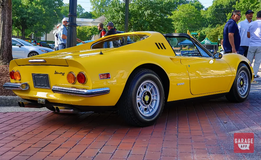 Rear three-quarter photograph of a Ferrari Dino 246 GT finished in Giallo Fly yellow, featuring sculpted rear fenders and classic Ferrari styling.