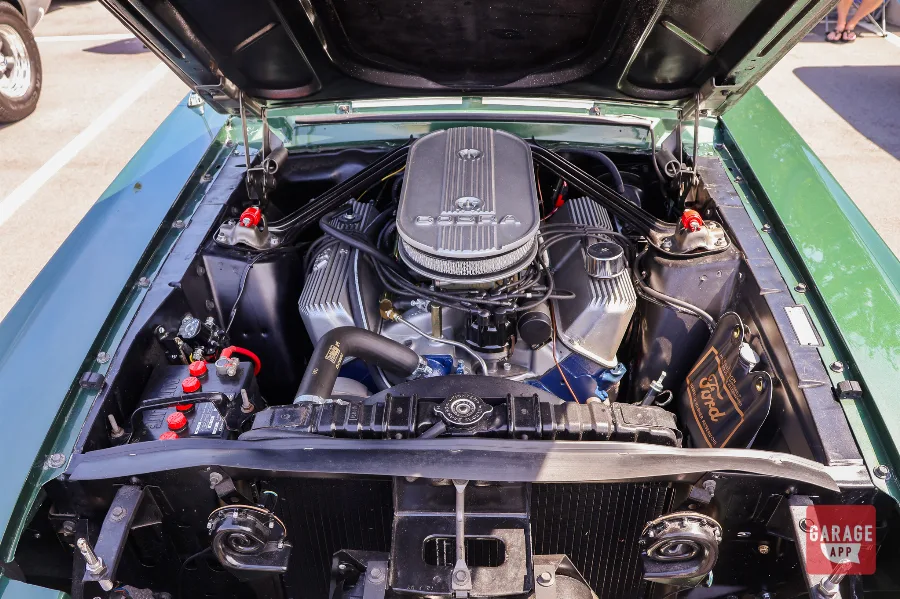 Engine bay of a dark green 1968 Shelby GT500 featuring its Cobra V8 engine displayed with the hood open.