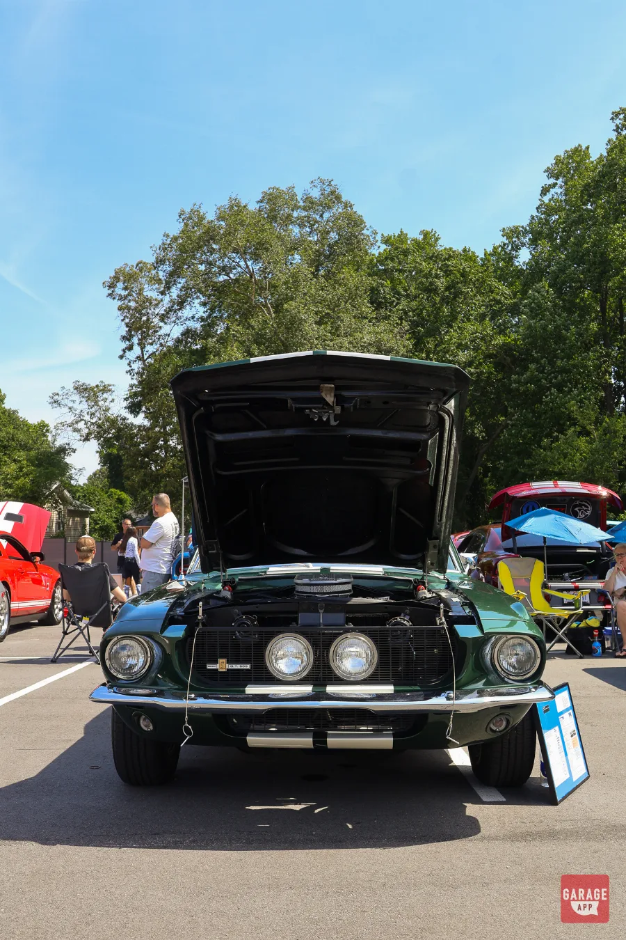Front view of a dark green 1968 Shelby GT500 displaying its open hood, grille-mounted driving lights, and Cobra V8.
