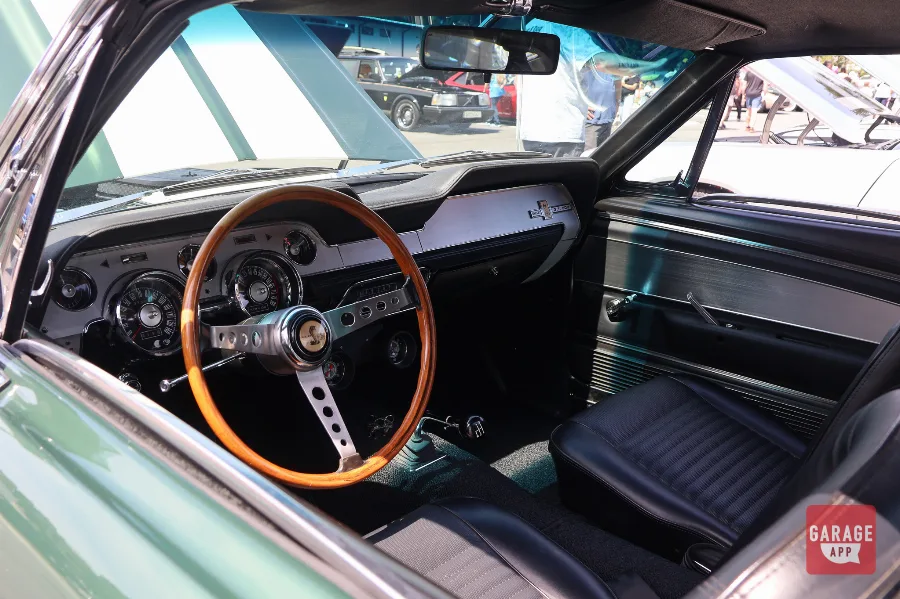Interior of a 1968 Shelby GT500 featuring a wood steering wheel, four-speed manual transmission, and classic Mustang dashboard.