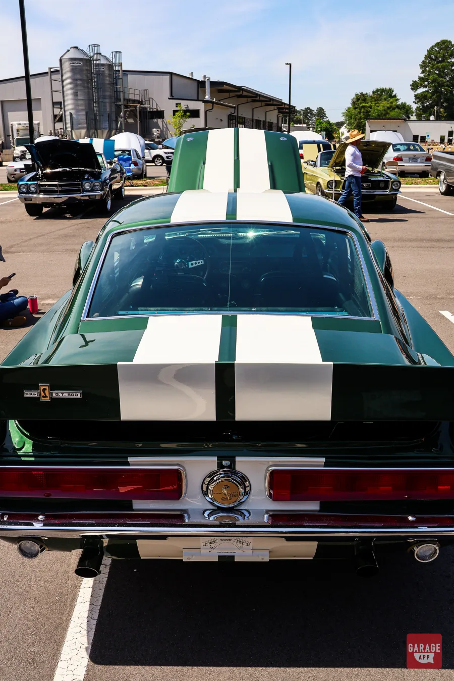 Rear view of a dark green 1968 Shelby GT500 highlighting white racing stripes and classic fastback styling.