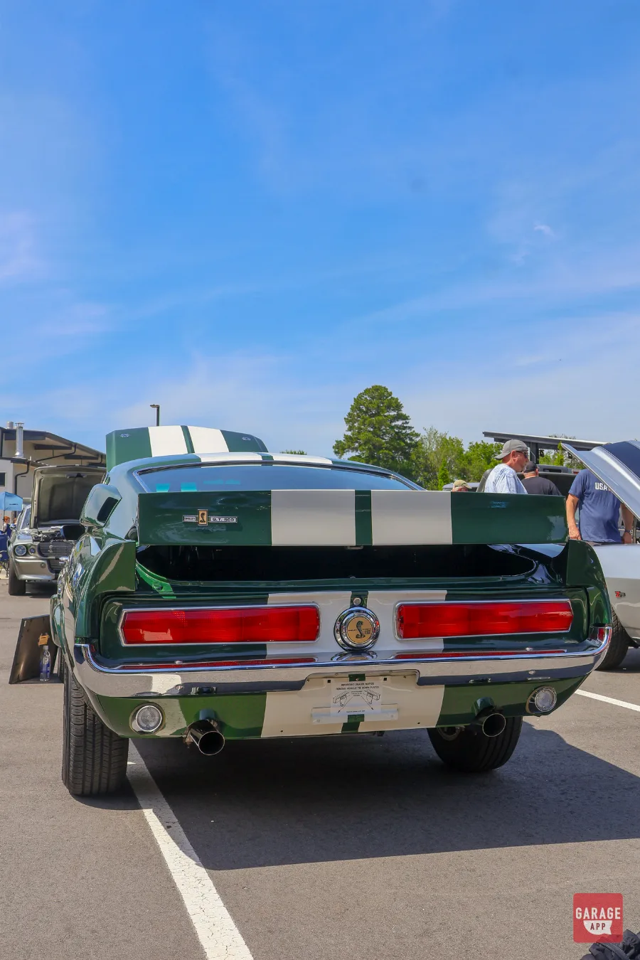 Rear three-quarter view of a dark green 1968 Shelby GT500 showing dual exhaust, spoiler, and Shelby Cobra badging.