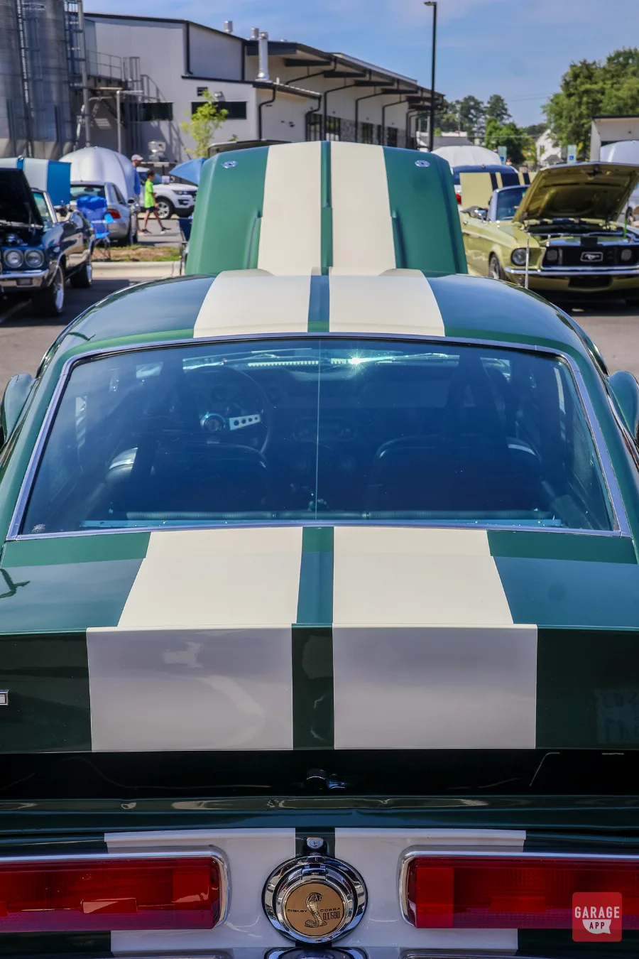 Rear window view of a dark green 1968 Shelby GT500 featuring white racing stripes extending across the fastback body.
