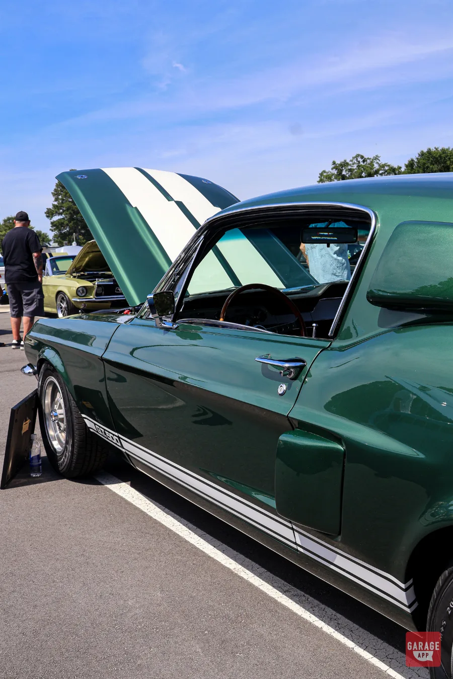 Side profile of a dark green 1968 Shelby GT500 with hood open, showcasing the classic fastback body and Shelby side scoops.