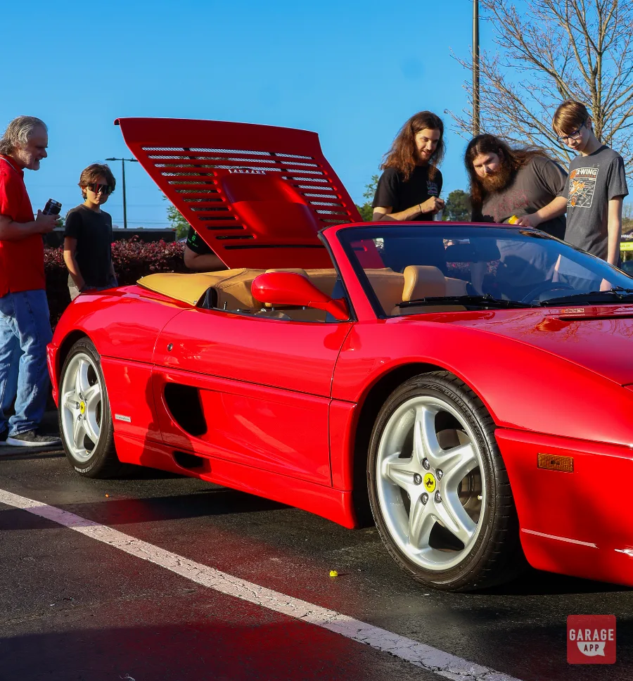 Side view of a red Ferrari F355 Spider convertible at a Cars and Coffee gathering.
