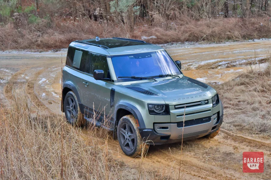 2024 Land Rover Defender 90 driving through muddy off-road trails with all-terrain tires in a forest adventure setting.