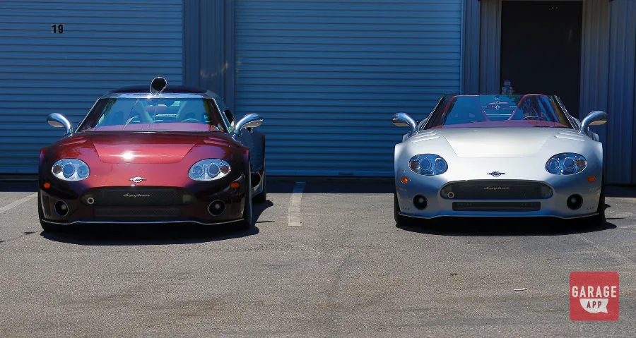 Front view of a 2009 Spyker C8 Laviolette and a 2006 Spyker C8 Spyder parked side by side outside Carolina Exotic Car Club.