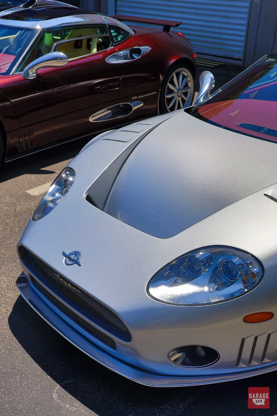 Close-up of the Champion Silver Spyker C8 Spyder with the Madeira Red C8 Laviolette in the background, highlighting handcrafted bodywork and aluminum details.