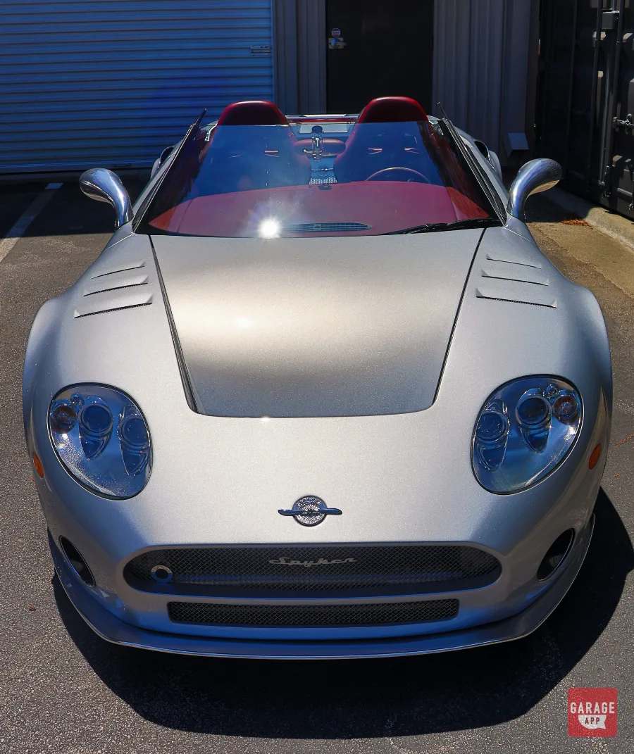 Close-up of the front end of a 2006 Spyker C8 Spyder in Champion Silver, showing the sculpted hood and handcrafted details.