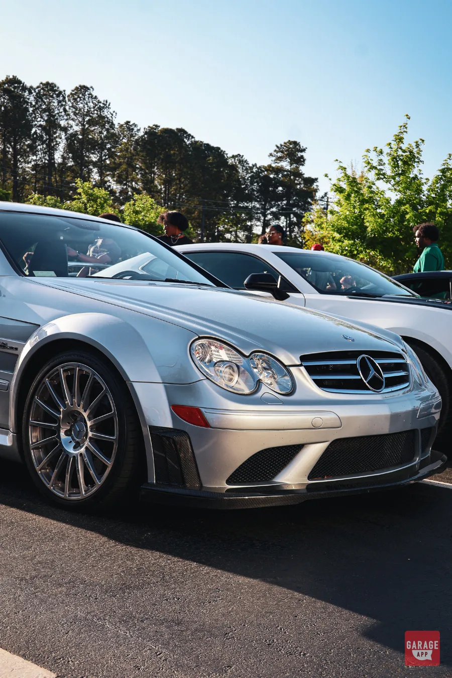 Low front three-quarter view of a 2009 Mercedes-Benz CLK 63 AMG Black Series in Iridium Silver Metallic, highlighting the carbon fiber front splitter and signature AMG styling.