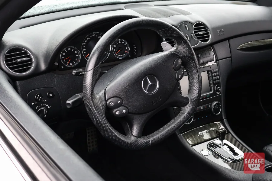 Close-up of the AMG steering wheel inside a 2009 Mercedes-Benz CLK 63 AMG Black Series, featuring paddle shifters, analog gauges, and a driver-focused cockpit.