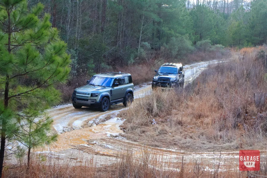 2024 Land Rover Defender 90 leading a lifted Toyota 4Runner along a muddy forest trail during an off-road adventure.