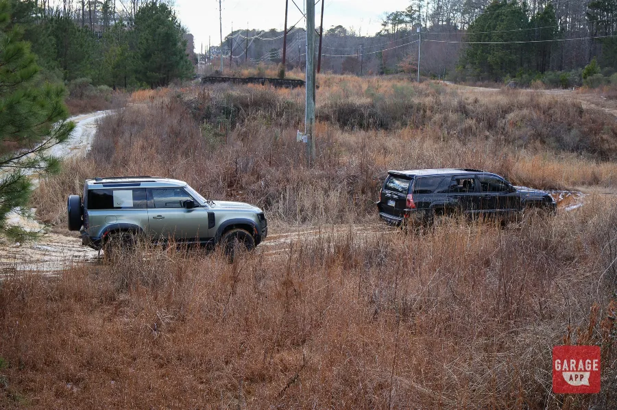 2024 Land Rover Defender 90 and lifted Toyota 4Runner navigating muddy off-road terrain through a wooded trail.