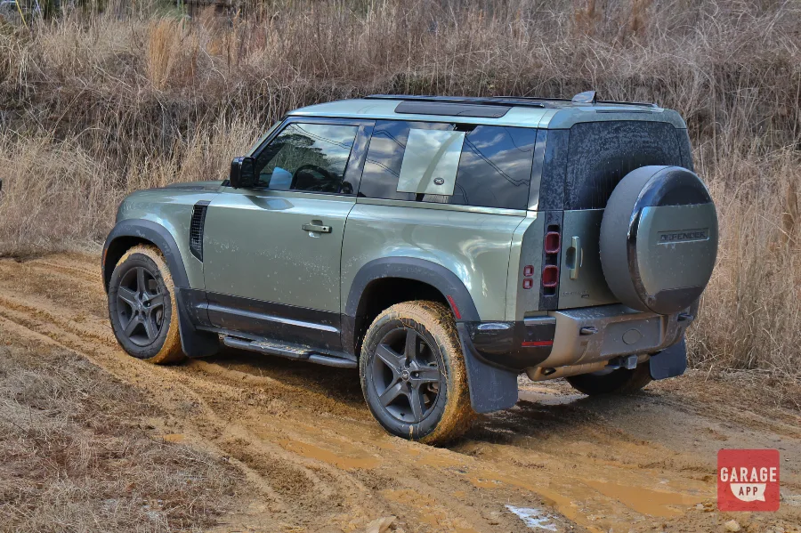 2024 Land Rover Defender 90 rear three-quarter view parked on muddy off-road trails after a forest drive.