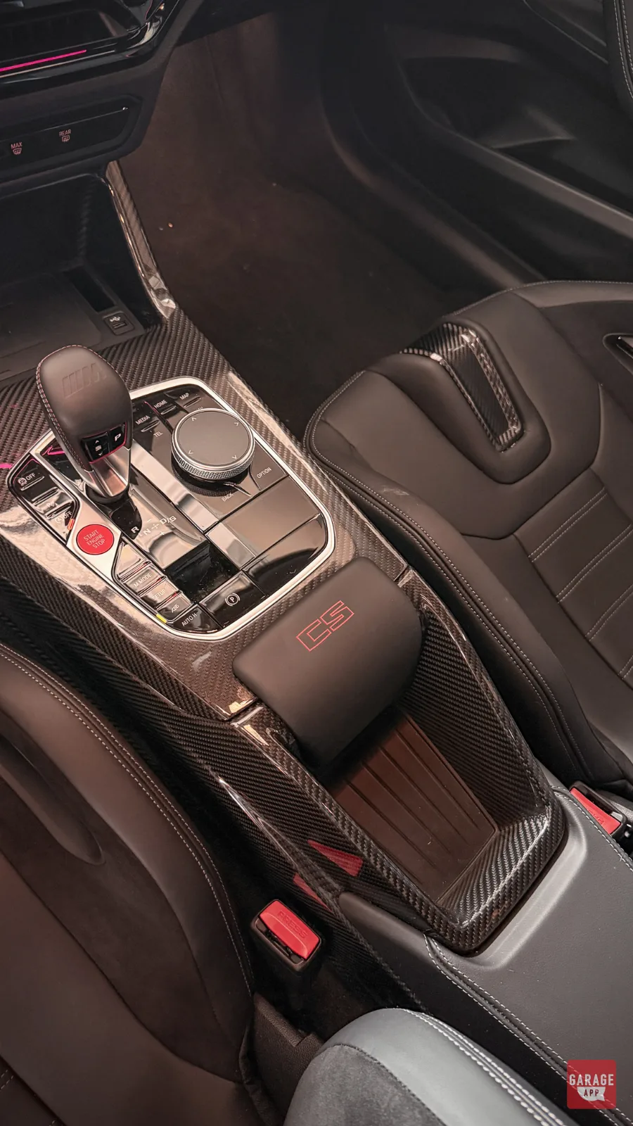 2026 BMW M2 CS interior featuring a carbon fiber center console, CS-branded armrest, M gear selector, and black leather sport seats.