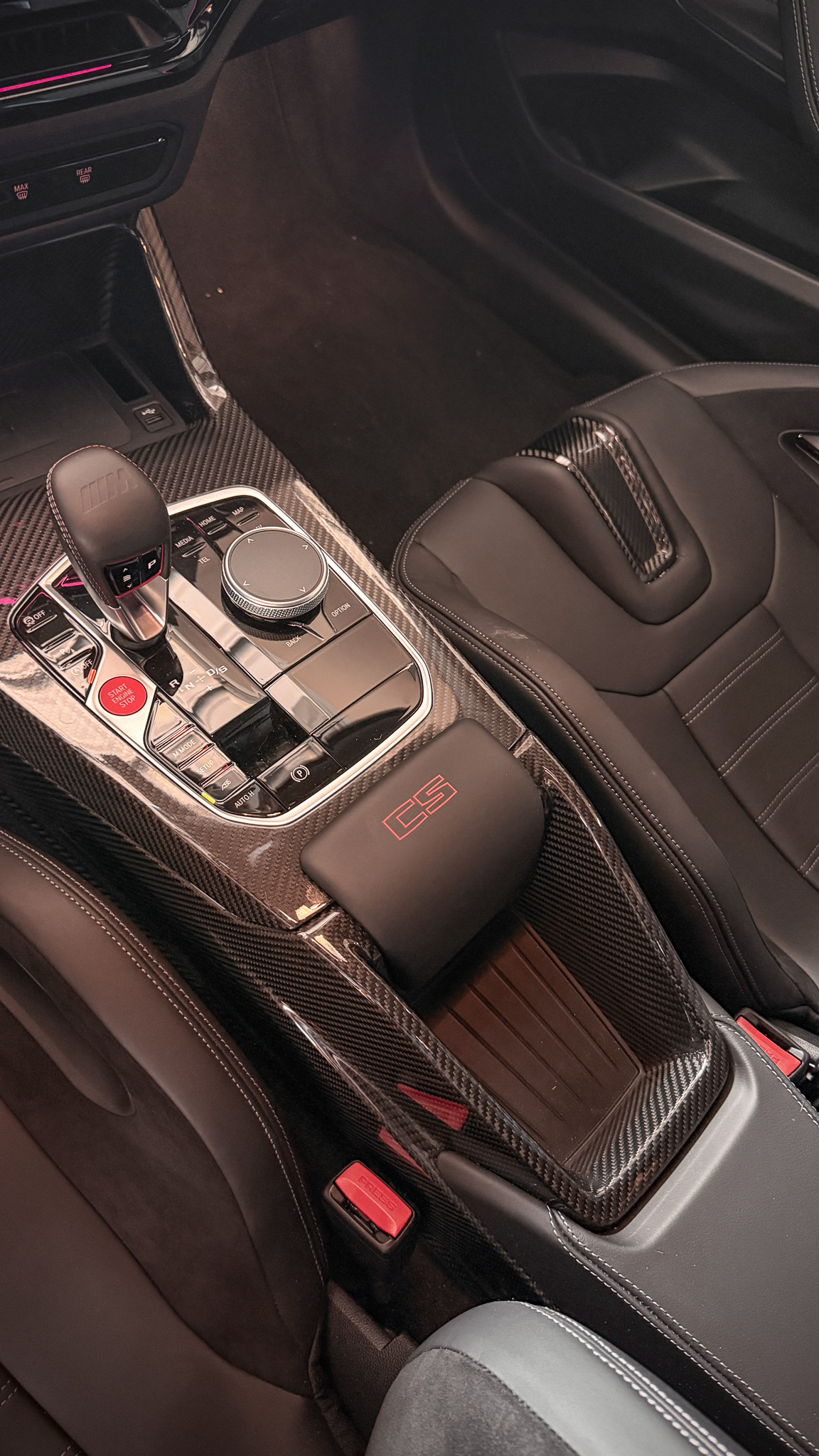 2026 BMW M2 CS interior featuring a carbon fiber center console, CS-branded armrest, M gear selector, and black leather sport seats.