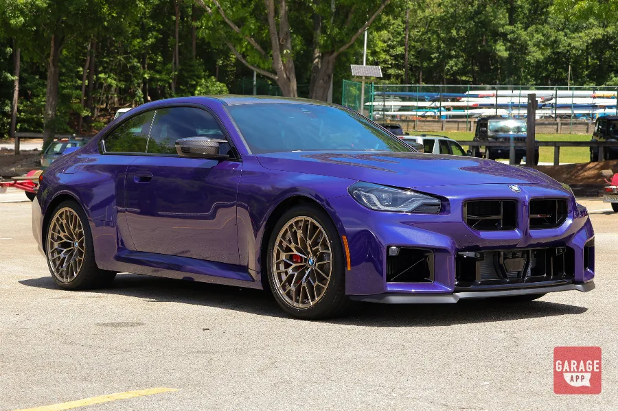 Front three-quarter view of a 2026 BMW M2 CS in Velvet Blue with carbon fiber accents and bronze wheels.