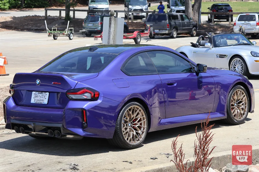 Close rear three-quarter view of a 2026 BMW M2 CS in Velvet Blue with quad exhaust tips and carbon fiber rear diffuser.