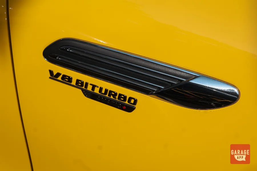 Close-up of the V8 Biturbo badge on a 2025 Mercedes-AMG SL 63 in MANUFAKTUR Sun Yellow, highlighting the handcrafted twin-turbo V8 and AMG performance heritage.