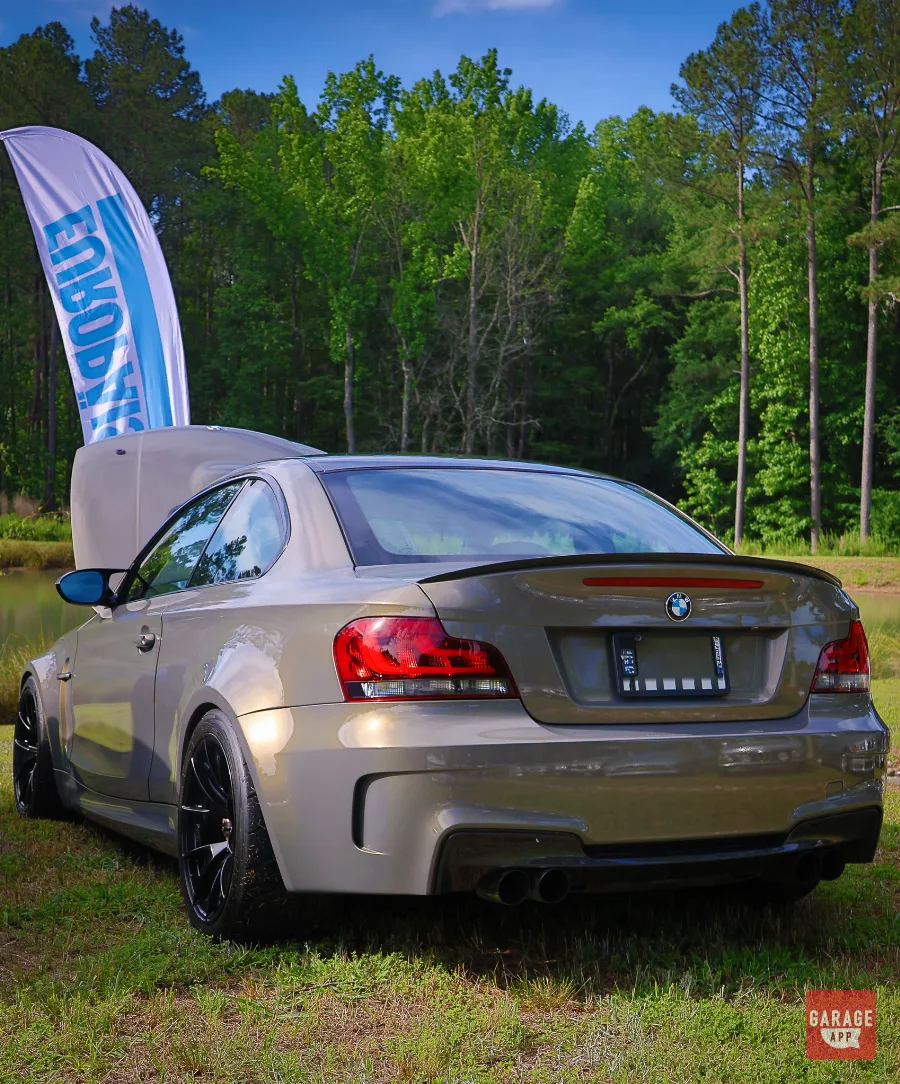 BMW 1M Coupe displayed at Europäisch surrounded by trees and European car enthusiasts at Silver Horse Garage.