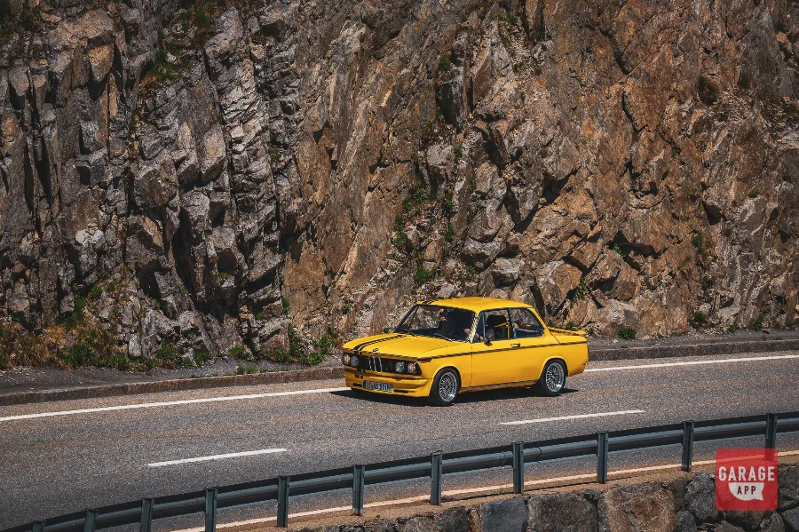 Yellow classic BMW 2002 driving Furka Pass Swiss Alps