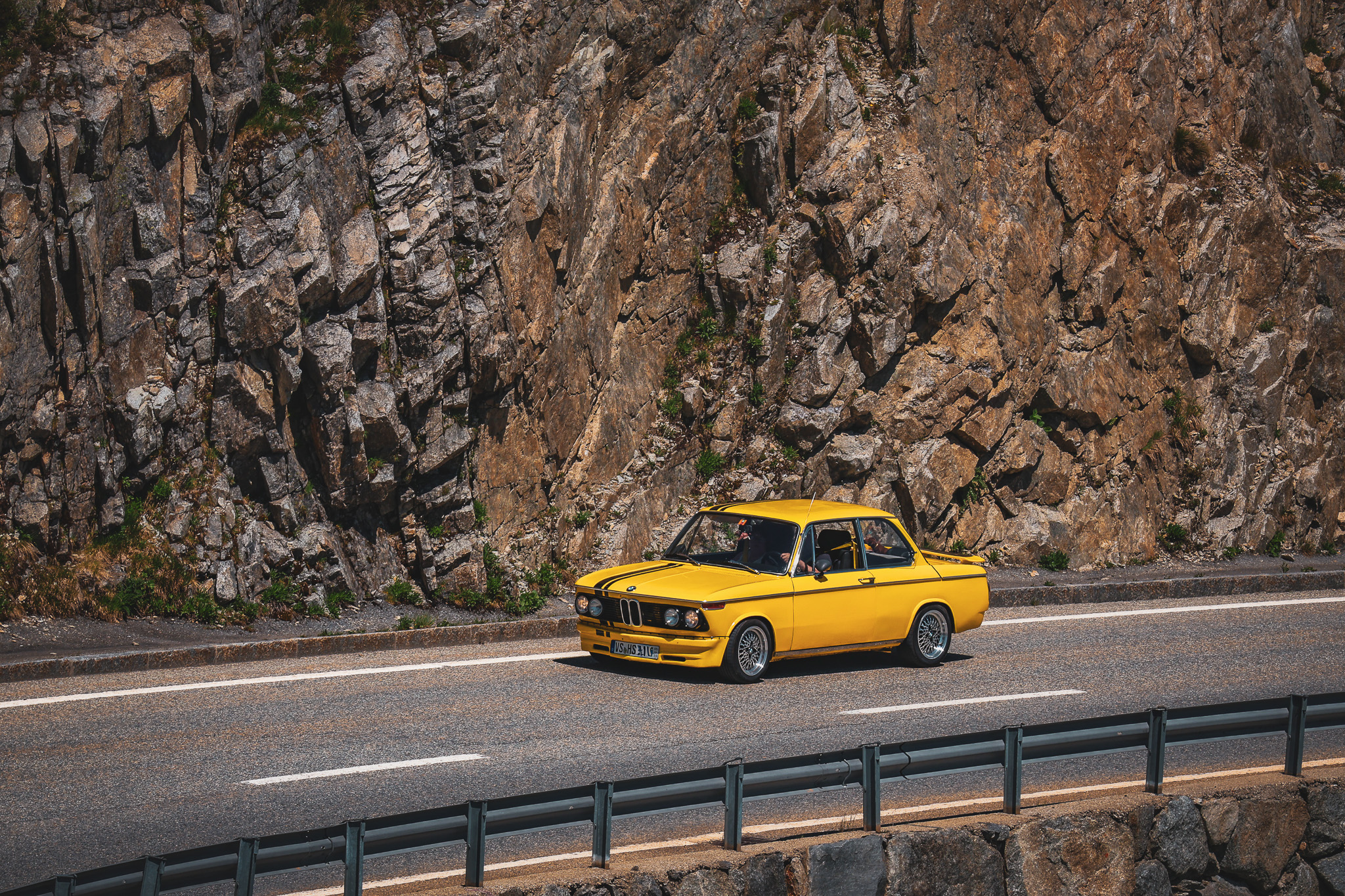 Yellow classic BMW 2002 driving Furka Pass Swiss Alps