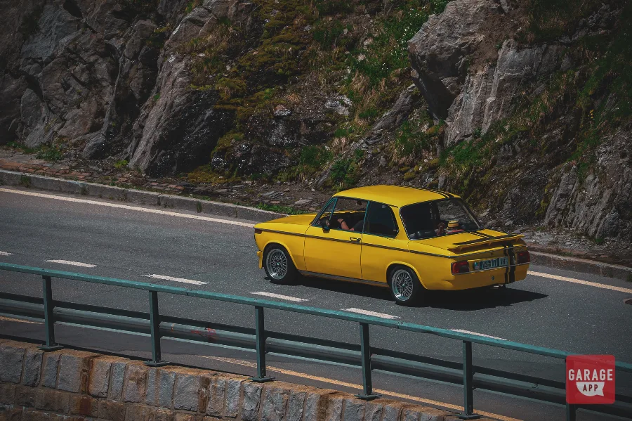 Yellow BMW 2002 rear three-quarter view Furka Pass road