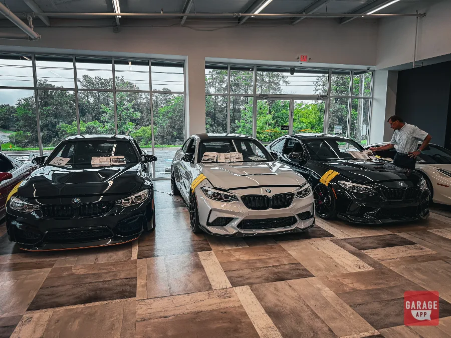 Black BMW M4, silver M2 CS, and black M2 lined up for sale in dealership showroom