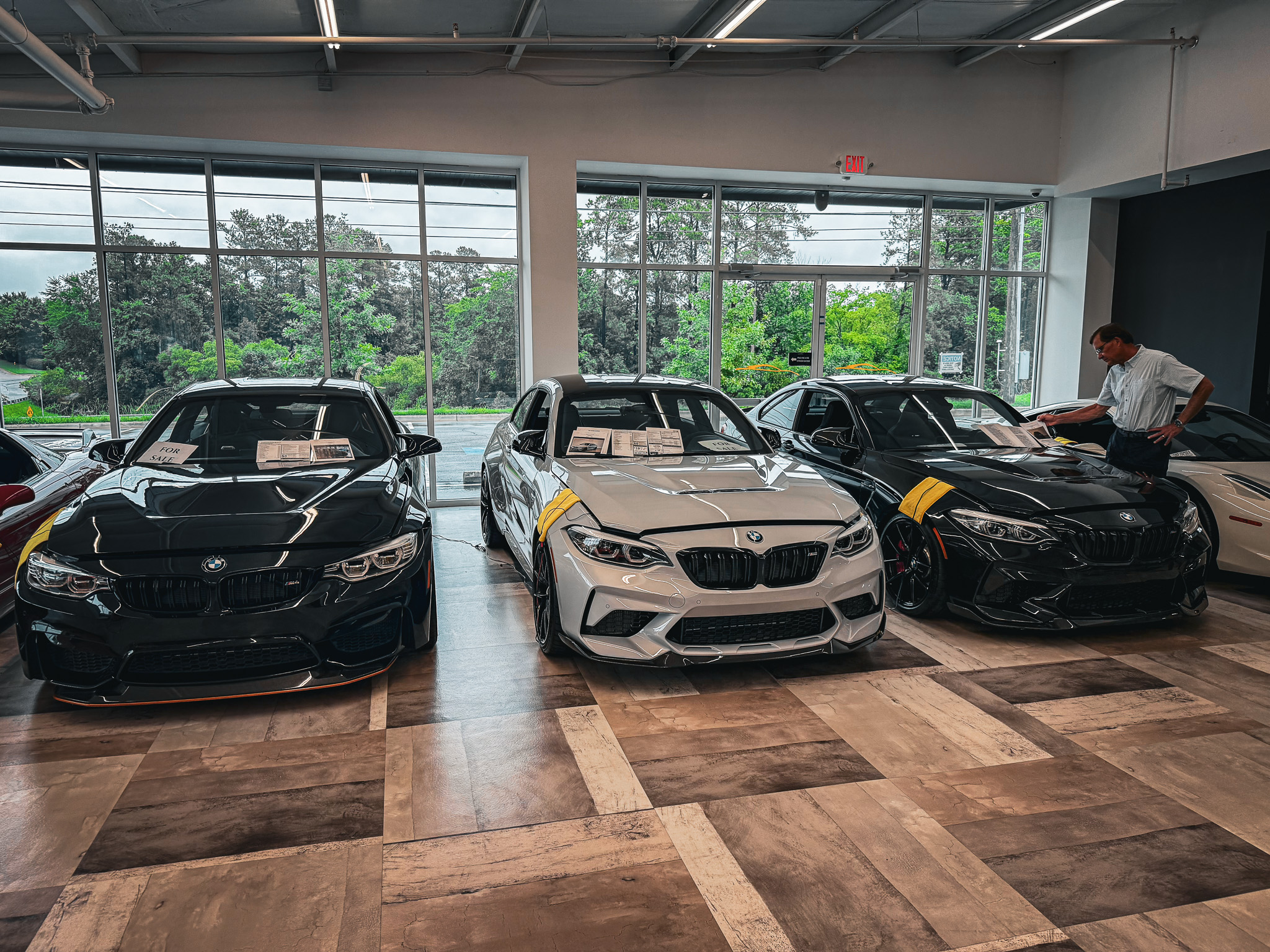 Black BMW M4, silver M2 CS, and black M2 lined up for sale in dealership showroom