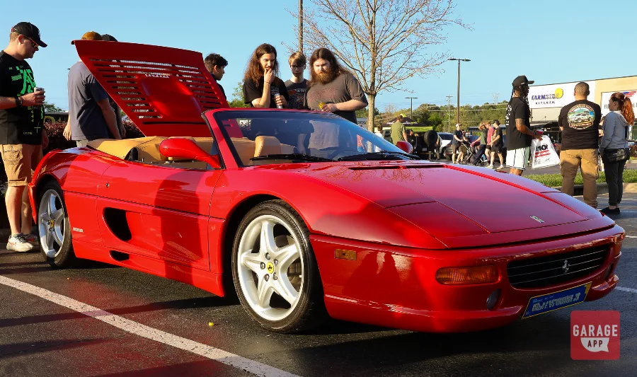 Red Ferrari F355 Spider convertible with the rear engine cover open at a Cars and Coffee event.