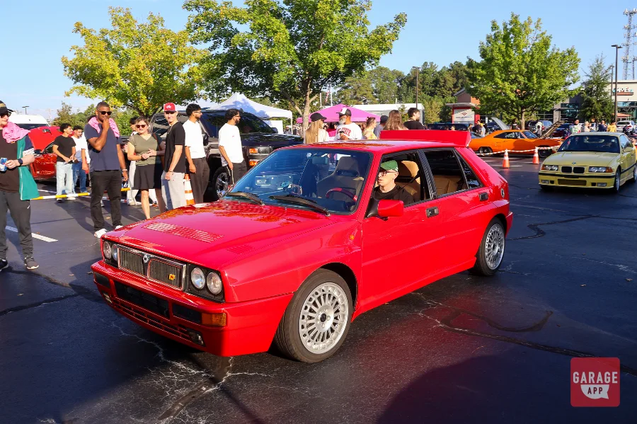 Red Lancia Delta HF Integrale driving through a crowded car meet lot