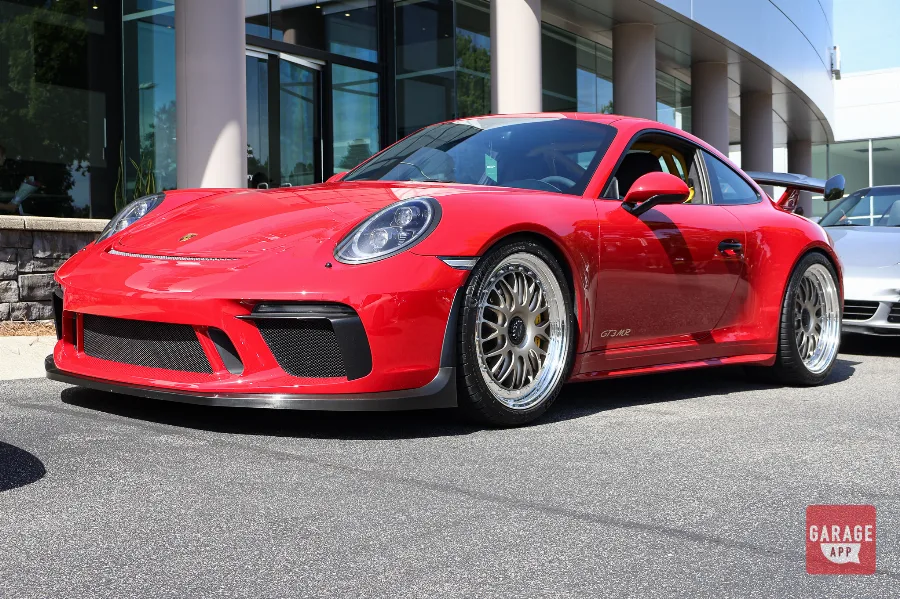 Guards Red Porsche 991.2 GT3 MR by Manthey Racing parked outside a Porsche dealership, showcasing the aggressive front fascia, lightweight wheels, and naturally aspirated 4.0-liter Porsche GT3 platform.