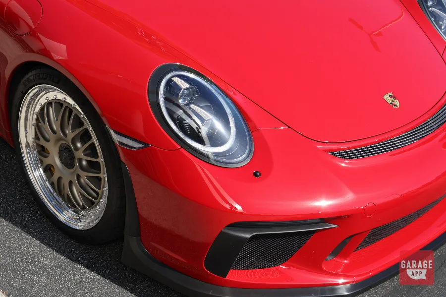 Detailed view of Porsche 991.2 GT3 MR headlights, forged wheels, front splitter, and Guards Red paint finish at a Porsche enthusiast event.