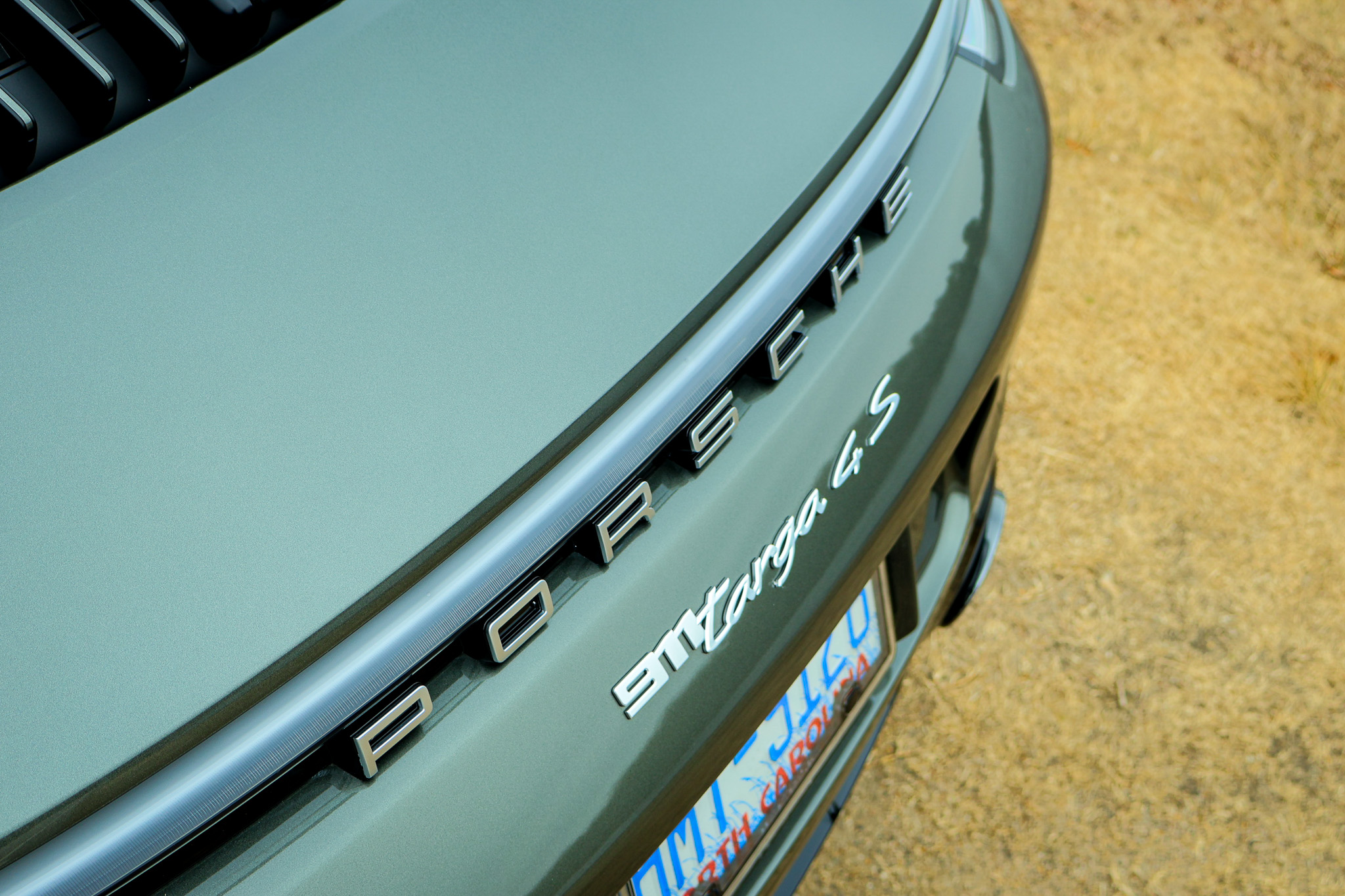 Close-up of the rear Porsche lettering on a 992.1 Porsche 911 Targa 4S finished in Aventurine Green Metallic, highlighting the full-width LED light bar.
