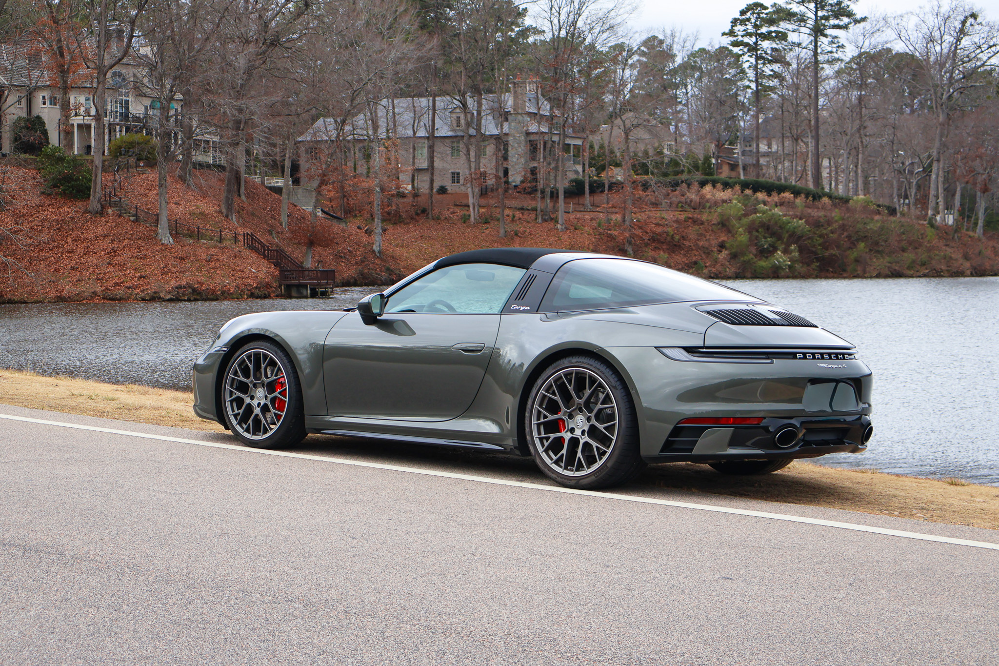 High front three-quarter view of a 992.1 Porsche 911 Targa 4S in Aventurine Green Metallic parked beside a scenic lakeside road.