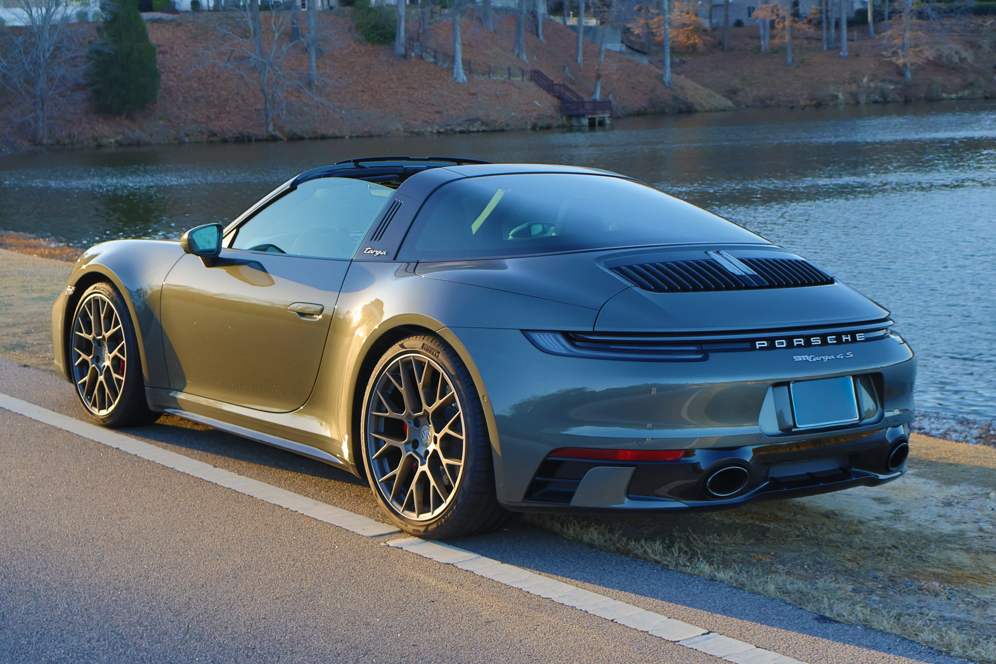 Rear three-quarter view of a 992.1 Porsche 911 Targa 4S in Aventurine Green Metallic with the automatic Targa roof in motion.