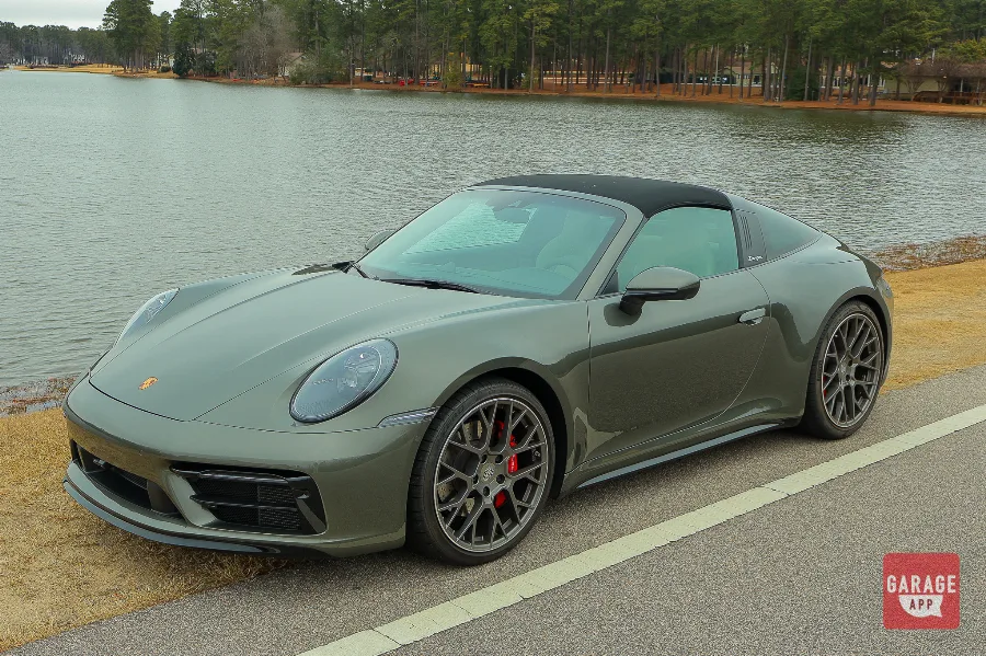 High front three-quarter view of a 992.1 Porsche 911 Targa 4S in Aventurine Green Metallic parked beside a scenic lakeside road.
