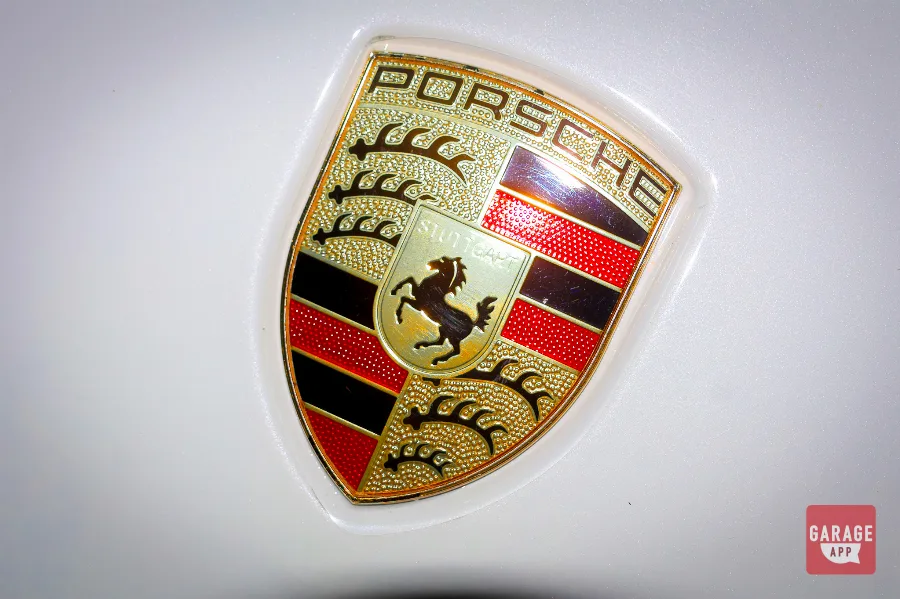 Close-up of gold Porsche crest emblem on white Macan S hood