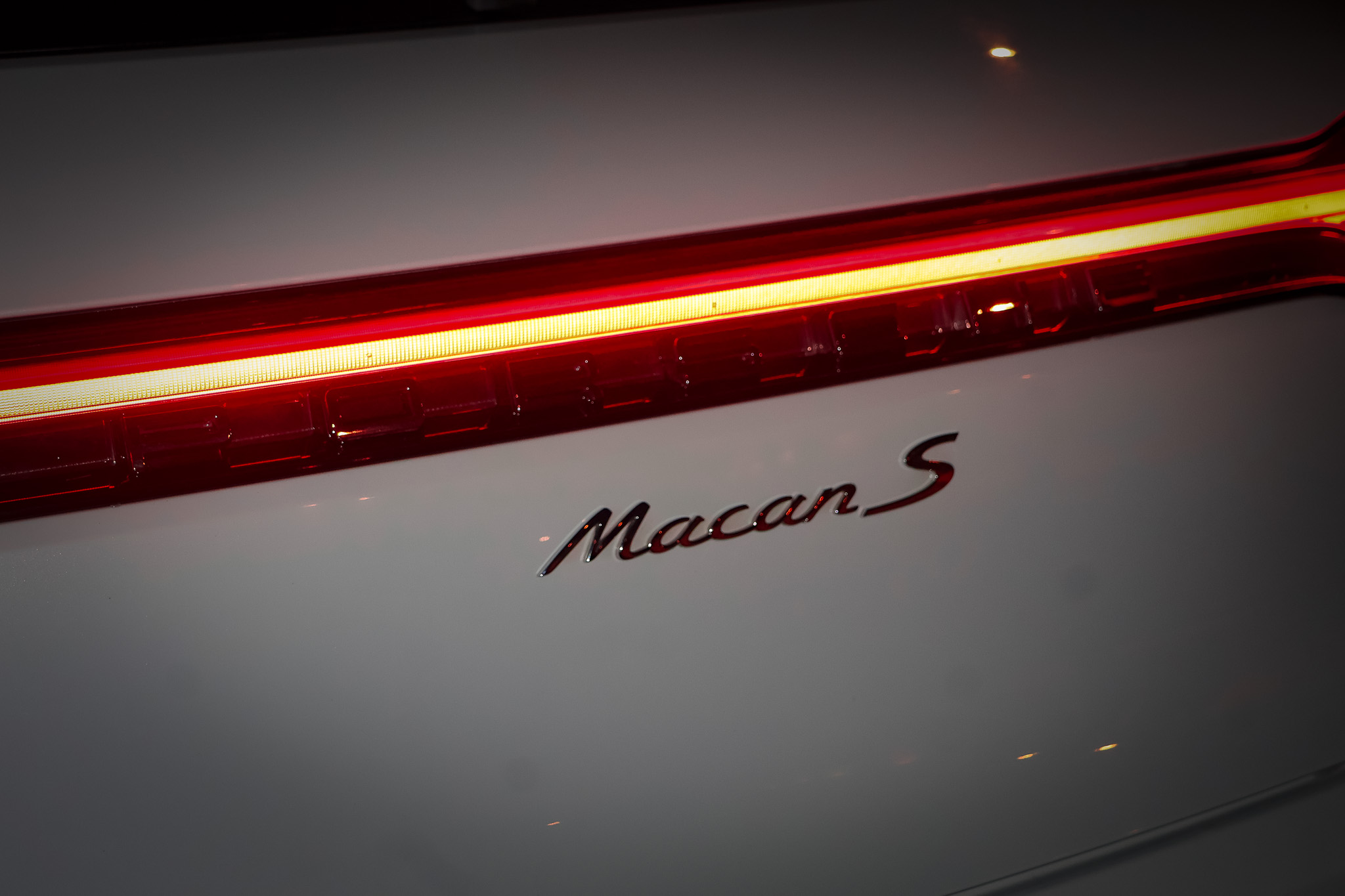 Illuminated LED taillight strip beside Macan S badge on white Porsche