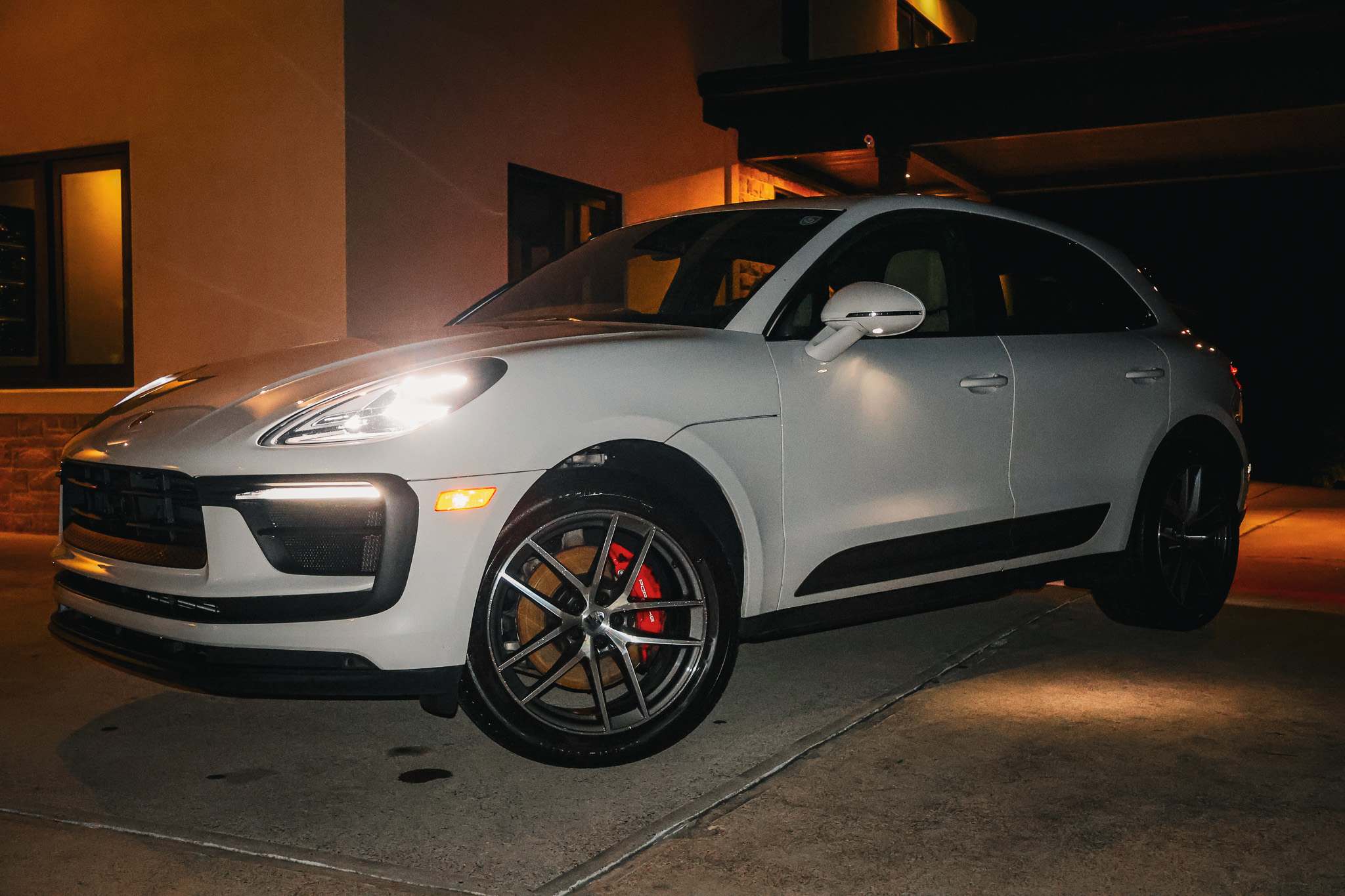 White Porsche Macan S front three-quarter view with LED headlights on at night
