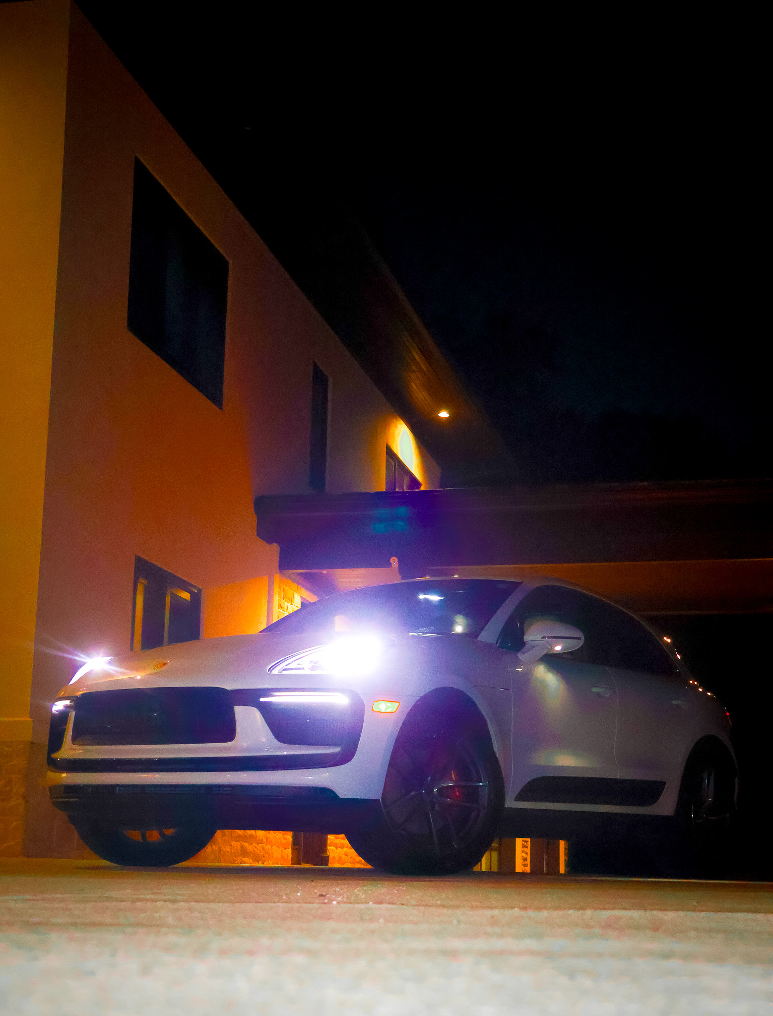 Low angle front view of white Macan S with bright LED headlights illuminated in driveway