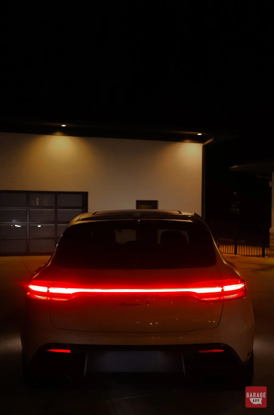 Straight-on rear view of white Porsche Macan S with full LED taillight bar lit at night