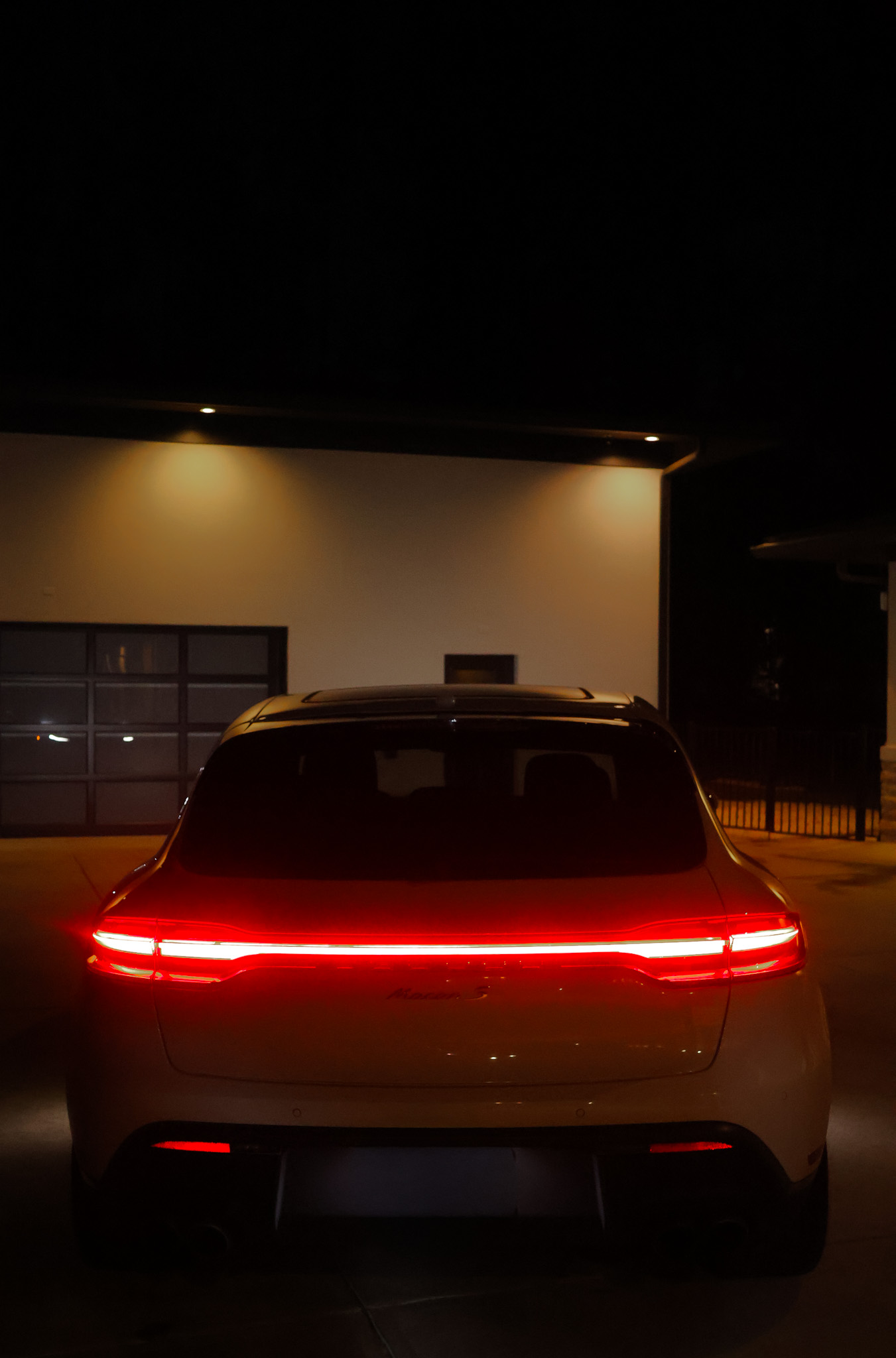 Straight-on rear view of white Porsche Macan S with full LED taillight bar lit at night