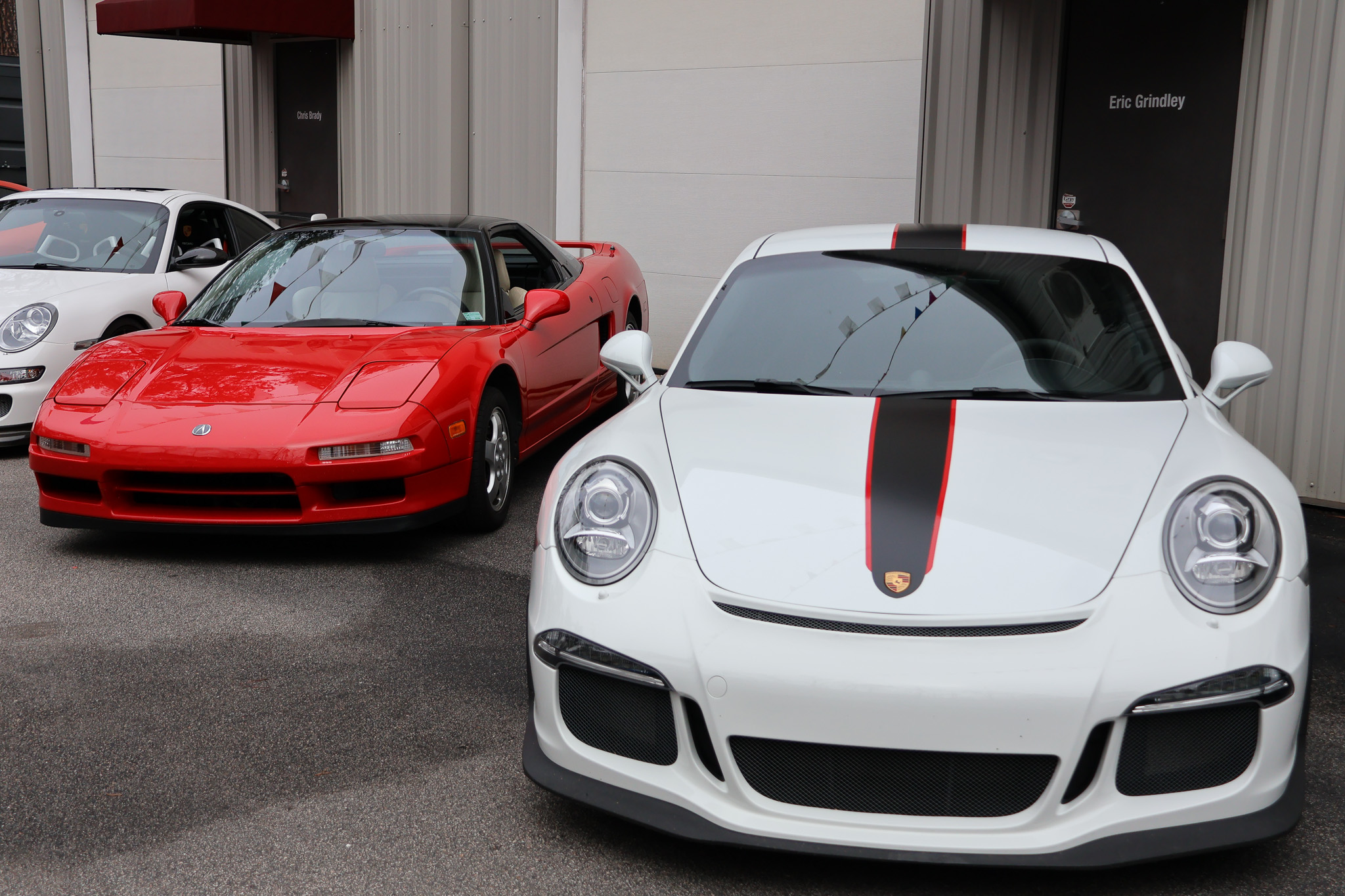 White Porsche 911 GT3 with red stripe parked beside red Acura NSX in garage